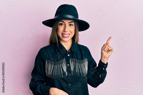 Young hispanic woman wearing cowgirl style smiling happy pointing with hand and finger to the side