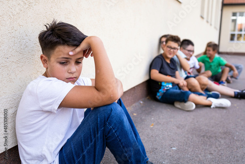 Group of schoolboys bullying a sad and upset looking boy.