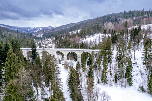 Wiadukt kolejowy w górach zimą nad rzeką i drogą. Wisła, Beskid Śląski w Polsce
