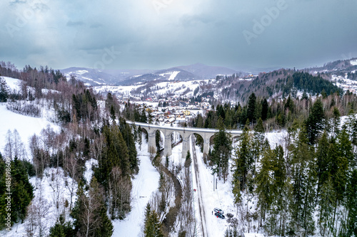 Wiadukt kolejowy w górach zimą nad rzeką i drogą. Wisła, Beskid Śląski w Polsce