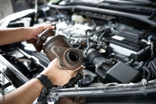 Close up old catalytic converter in hand Car service man remove from engine gasoline car dust clogged condition on filter in service concept and engine room in the background