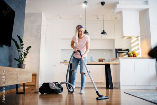 A smiling woman vacuuming living room floor at her home.