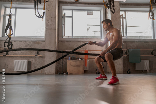 Side view of handsome physically fit male working out with heavy ropes in cross fit gym