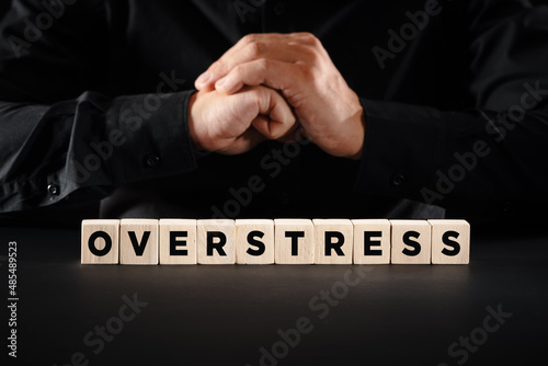 Emotional stress concept. Man with clasped hands with the word overstress on wooden blocks.