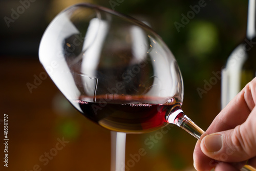 Wine tasting. A glass of red wine on the background of a restaurant table with bottle at an evening dinner or event party.