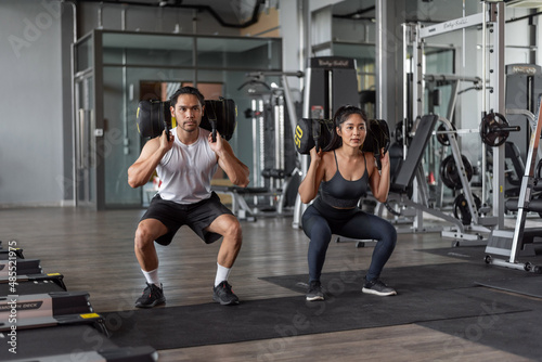 Asian woman and asian man exercise in fitness. Healthy couple doing squat exercise together in gym.