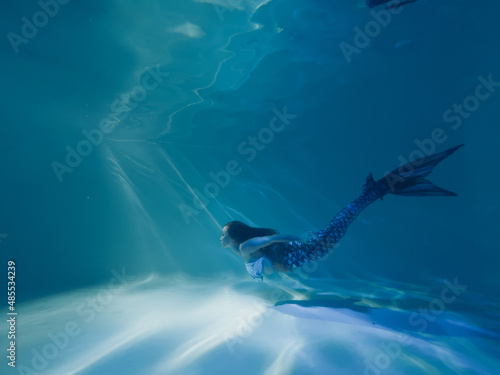 Woman with mermaid tail swims and dives underwater.