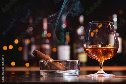 Glass of whiskey or cognac with ice cubes and smoking cigar