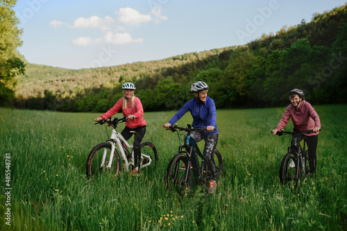 Happy active senior women friends cycling together outdoors in nature.