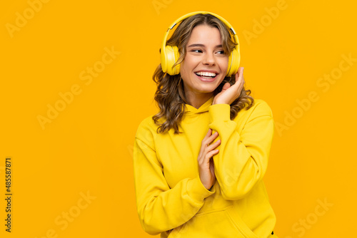 smiling attractive woman listening to music in headphones on yellow background