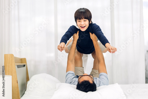Portrait of enjoy happy love asian family father carrying little asian boy son smiling playing superhero and having fun moments good time on bed at home