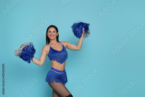 Beautiful cheerleader in costume holding pom poms on light blue background. Space for text