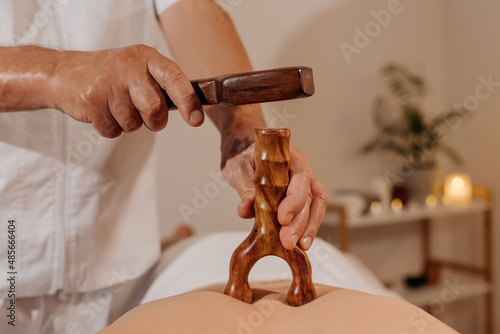 Close-up man's back during traditional thai tok-sen massage. Oriental alternative medicine with wooden tools. Body care and SPA in Thailand resort.