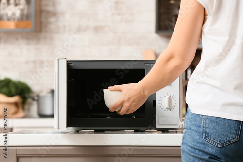 Woman putting bowl with food into microwave oven in kitchen, closeup