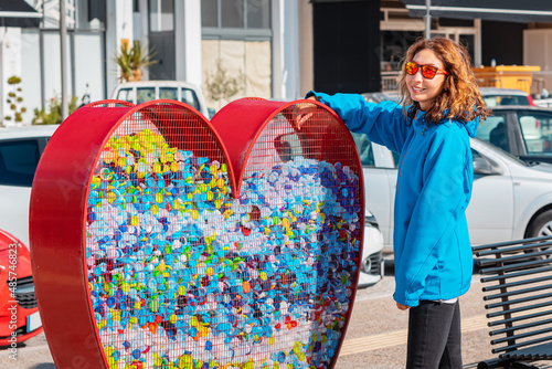 responsible girl hands over the plastic for recycling in a heart-shaped container installed by the authorities on the city street. Awareness and sustainability