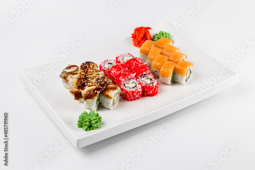 Set of different sushi rolls with rice, fish, cucumbers, wasabi, ginger, caviar and sesame. Large white plate on a white background. Lots of sushi in one dish.