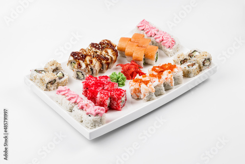 Set of different sushi rolls with rice, fish, cucumbers, wasabi, ginger, caviar and sesame. Large white plate on a white background. Lots of sushi in one dish.