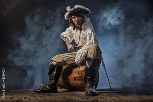 Pirate filibuster sea robber in suit with gun and saber sits on barrel. Concept photo