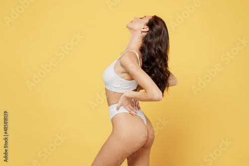 Side profile view sexy stunning attractive young brunette caucasian woman 20s wearing white underwear with perfect fit body standing posing isolated on plain yellow color background studio portrait
