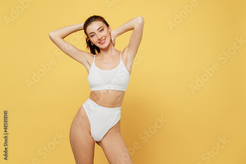 Smiling lovely attractive young brunette woman 20s wearing white underwear with perfect fit body standing ties hair in ponytail look camera isolated on plain yellow color background studio portrait