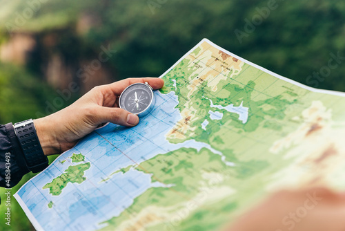 Compass and map in hands of traveler for checking and searching position and direction at the top of peak of mountain while hiking for camping