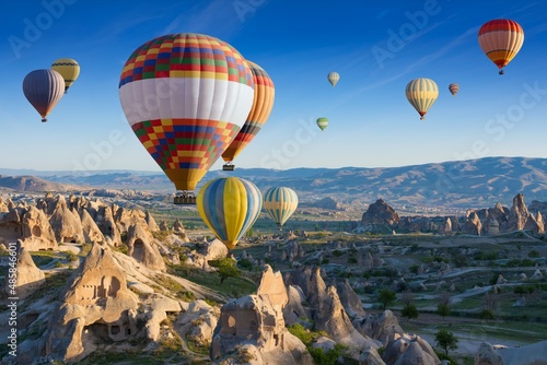 Colorful hot air balloons fly in blue sky over amazing rocky valley in Cappadocia, Turkey.