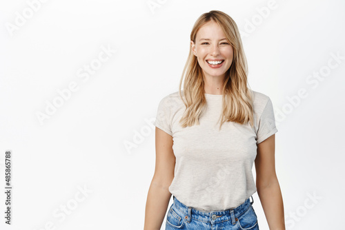 Portrait of happy smiling woman showing white smile, laughing and looking carefree at camera, standing over white background