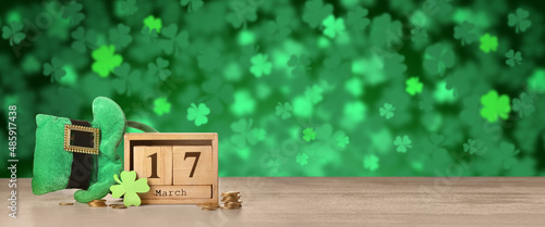 Leprechaun's hat, calendar and coins on table against green background. St. Patrick's Day celebration