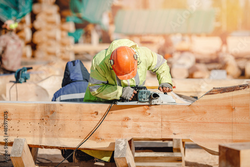 Industrial work carpenter grinds log with electric jointer, construction frame building site of house made of wood