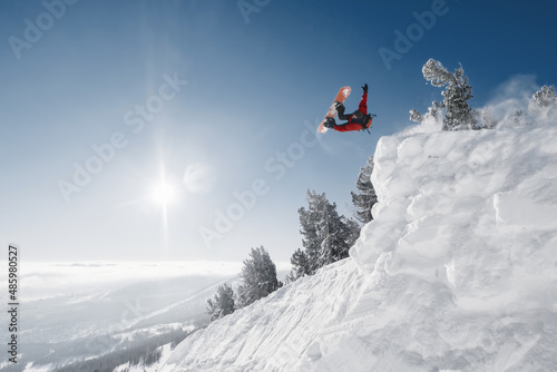 Snowboarder making high jump in clear blue sunny sky above mountains