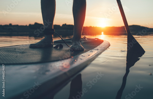 Close up of man paddleboarding at sunset lake