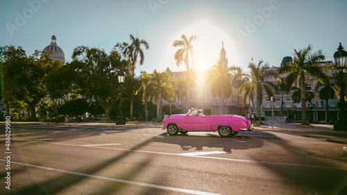 Havana, Cuba. Różowy cabriolet w świetle zachodzącego słońca. Jedzie ulicą miasta pod palmami i niebieskim niebem