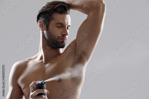 Young confident man applying deodorant on his body