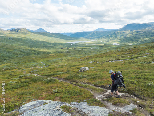 Lonely man hiker figure with backpack and fishing rod at Lapland landscape with green valley, mountains and winding river stream. Wild nature at Padjelantaleden hiking trail. Summer day