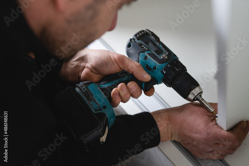 One man caucasian male using electric cordless screwdriver drill assembling furniture at home DIY carpenter at work