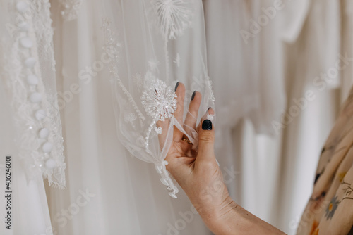 Closeup of a woman looking at a wedding dress, touching gown sleeve manually embroidered, at a wedding showroom.