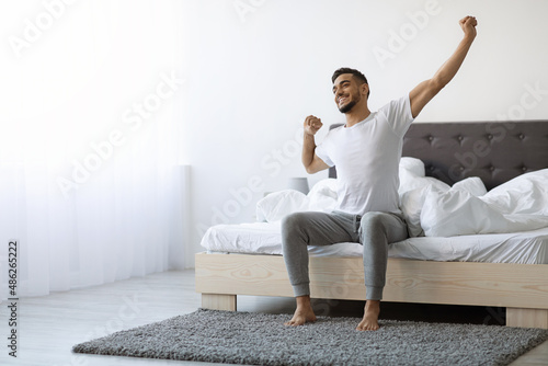Good Morning. Happy Arab Guy Sitting On Bed And Stretching After Sleep