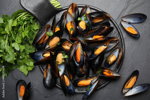 Serving board with cooked mussels and parsley on slate table, flat lay