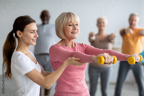 Young lady coach helping senior woman while exercising