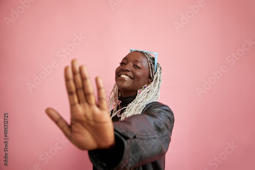 Studio portrait of smiling woman with bleached braided hair showing stop gesture