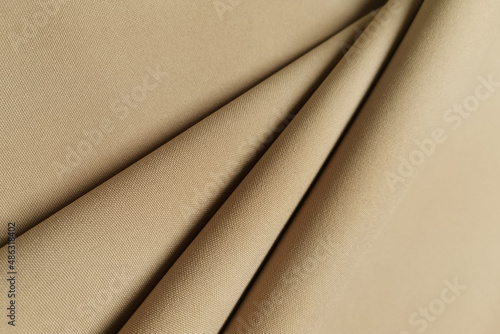 Gold crumpled or wavy fabric texture background. Golden abstract linen cloth soft waves. Gabardine wool fabric. Merino yarn. Smooth elegant luxury cloth texture. Concept for banner or advertisement.