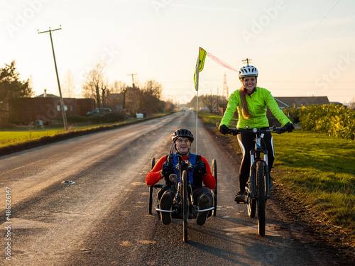 Woman riding bike and disabled man riding handcycle on country road