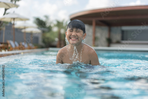Asian Young Boy Having a good time in swimming pool, He Jumping and Playing a Water in Summer.
