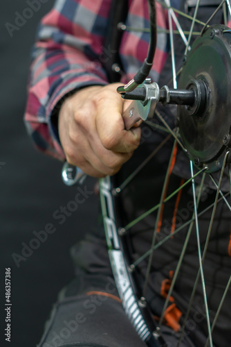 Repair of electric bicycles. A bicycle mechanic holds a wheel with an electric motor and a wrench in his hands. Bicycle wheel close-up on a black background.