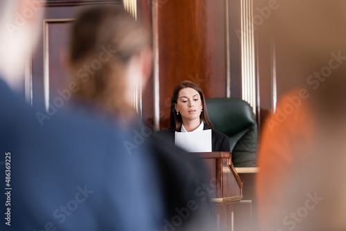 prosecutor reading lawsuit in court near people on blurred foreground