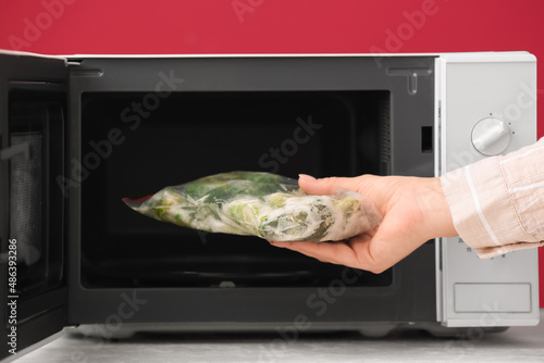Woman putting package with frozen vegetables into microwave oven, closeup