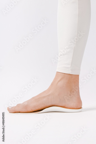 Medical insoles. Isolated orthopedic insoles on a white background. Treatment and prevention of flat feet and foot diseases. Foot care. Insole cutaway layers. Leg hanging over the insole.