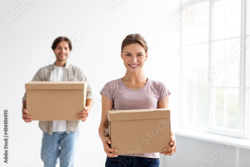 Happy millennial european male and woman carry boxes with stuff, enjoy moving to new apartment