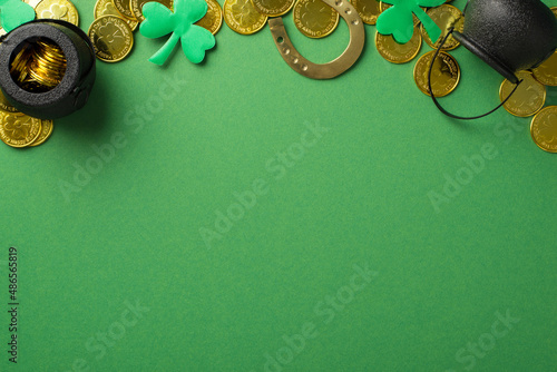 Top view photo of the many golden coins two black pots with money bronze horseshoe and confetti in shape of clovers at the top of the green empty isolated background