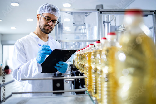 Food factory worker taking notes and controlling production line of edible oil.